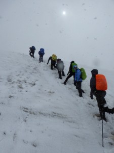 My only group tour, climbing a wall of snow on the Laugavegur Trail. There's no borderline between the snow wall and the white sky. The rest of the group are mostly carrying colourful backpacks. It's June.