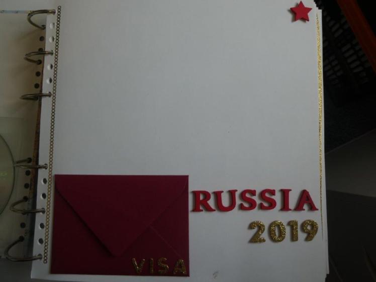 Title page of my Russia scrapbook. It's a bit bare - it has Russia 2019 spelled out in red and gold stickers, a wooden star in the top corner, a big empty space at the top and a small red envelope at the bottom. The word VISA is stuck on the envelope in gold letters.