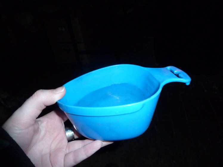 An odd-shaped blue plastic camping cup full of water being held up against a dark background.