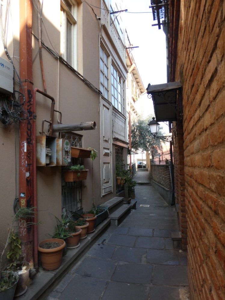 Narrow streets in the Old Town. The house on the left has lots of plants out on its narrow ledge as well as hardware for the heating and air conditioning inside.