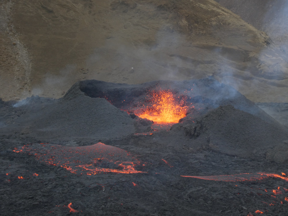A close-up of the Meradalir eruption: a small black crater with fire dancing around in the middle.