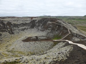 Standing on top of one of the Grabrok craters. There's a wooden boardwalk with stairs leading around the edge of the crater rim and you can also walk right down into the crater itself. The whole thing is red rock but it's so covered in greyish-green moss that you can't see a lot of the bare rock.