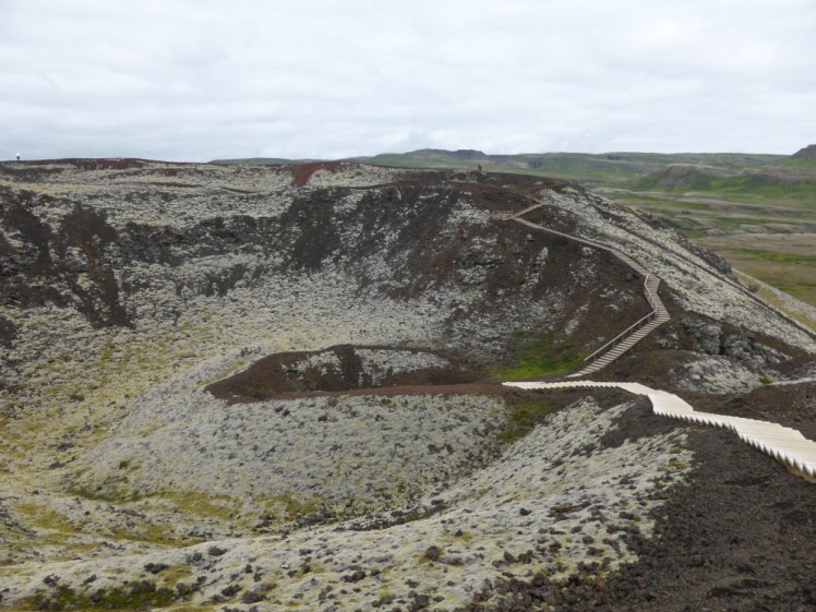 Standing on top of one of the Grabrok craters. There's a wooden boardwalk with stairs leading around the edge of the crater rim and you can also walk right down into the crater itself. The whole thing is red rock but it's so covered in greyish-green moss that you can't see a lot of the bare rock.