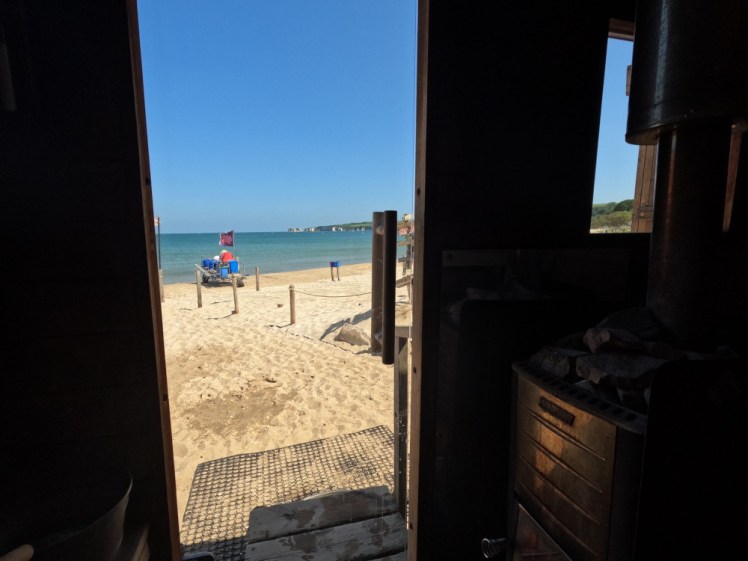 The view from the sauna hut. You can see the woodburner in the shadows of the shed but mostly you can see sunshine and beach and blue sea through the glass door.