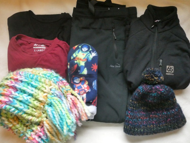 What I'm wearing - a black thermal top, a red t-shirt, a pair of black outdoors trousers, a smooth black fleece, all folded nicely on a white blanket. On top of the pile is a blue bobble hat, a pair of fleece mittens with astronauts on and a colourful scarf.