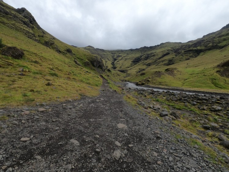 A steep-sided green and black valley with a stream bubbling down the right-hand side. It looks like the valley closes up just ahead and there's no way there's room for a swimming pool here...