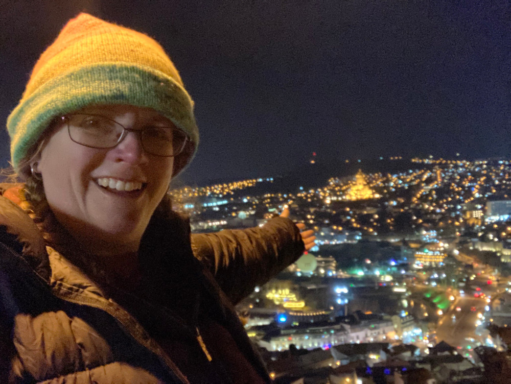 Me at the Mother of Georgia taking a night selfie with Tbilisi, wearing the stripy hat and my black down jacket.