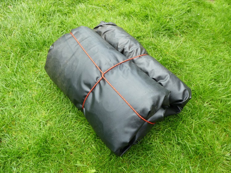 A bedding roll made of a black groundsheet and tied with red cord. Its ends are neatly folded up and the knot is on the bottom today.