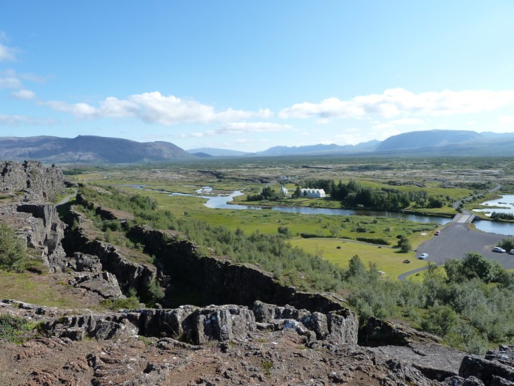 Þingvellir on a summer day, looking across the rift valley from the viewpoint, with cliffs in the foreground and a snow-covered shield volcano in the distance.