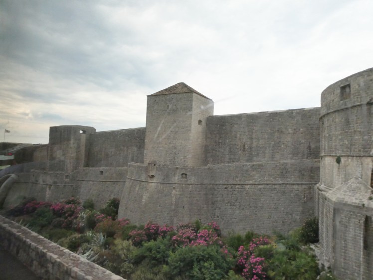 The very high, very solid grey stone walls of Dubrovnik seen from the airport bus driving past the outside.