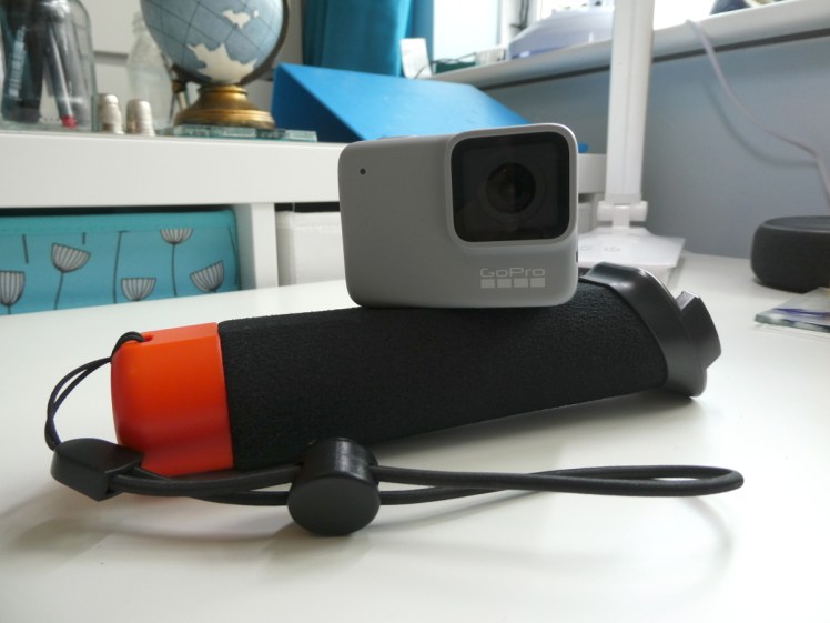 GoPro Hero7 White - small rectangular off-white camera, perched on top of a foam handle that can float even with the camera on the end of it.