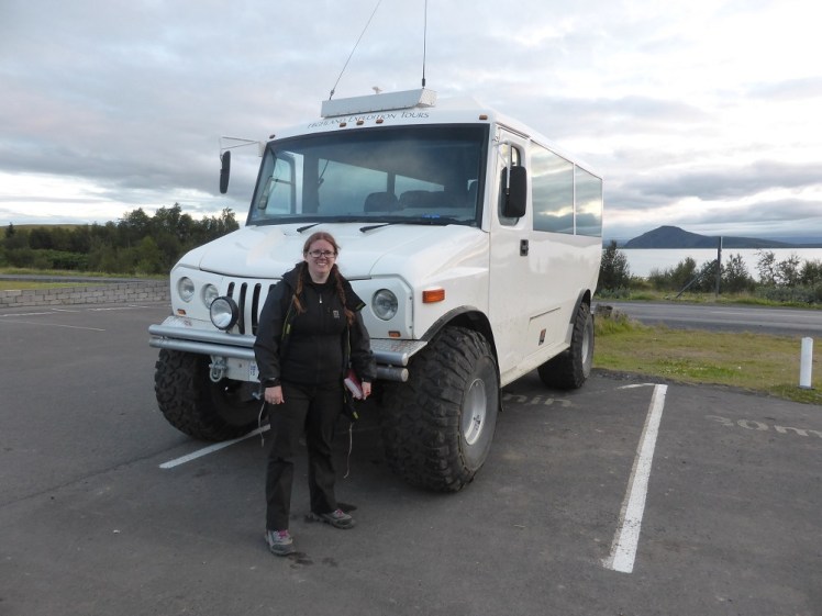 Me, all in black warm clothes, standing in front of a huge white boxy jeep. Behind us is the lake and a mountain. The sky is overcast but bright. It's at least 10pm.