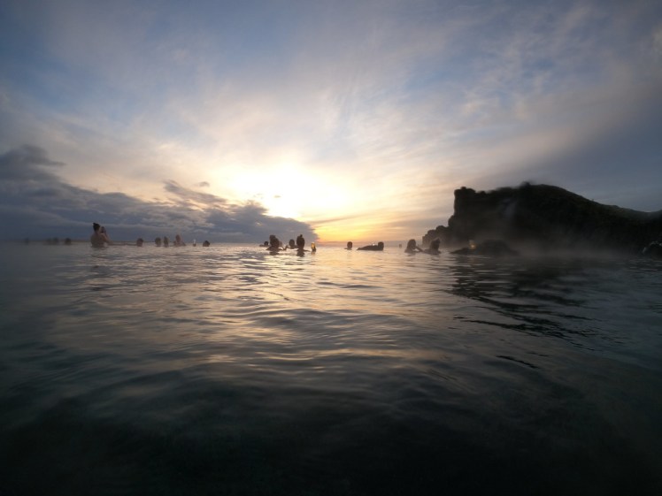 The sunset as seen from the Sky Lagoon, turning the sky bright yellow and peach against the cliff walls of the Sky Lagoon.