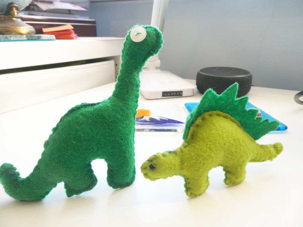 Two smallish dinosaurs made of green felt with buttons for eyes. They're pretty much 2D but standing up thanks to hidden cocktail sticks.