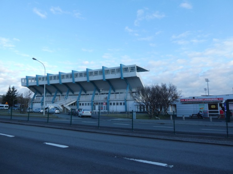 Laugardalslaug from across the road; a big blue and white stadium side towering over a pool that you can't see from here, with a hot dog kiosk right outside.