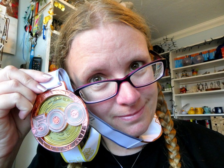 Selfie with my 500km medal. It's huge, a big copper-coloured disc with a copper-coloured 500 across the middle and a gold spinning centre with footprints on it