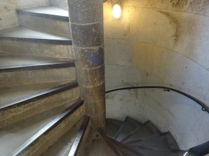 Stone spiral stairs, going clockwise. These date to the 1870s, so they're still nice and square and they have edging on each step to help prevent wear. They're lit by electric light and there's clearly some natural light coming from a window out of shot at the top.