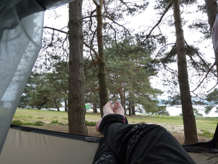 My feet, sticking out of the tent door. Beyond are pine trees and beyond them, a glimpse of the sea.