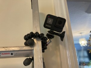 My GoPro Hero 8 Black attached to a small Gorillapod with a tripod adaptor. The tripod's ball-joint legs are wrapped around the side of a ladder leaning against a wall on my landing. It's counting down from a three second timer photo.