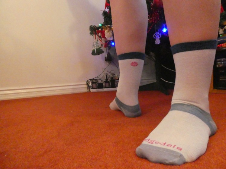 My feet in pale blue thin liner socks. My left foot is close to the camera so you can see the markings on the front of the sock. My right foot is turned so you can see the pink daisy on the back of the cuff.