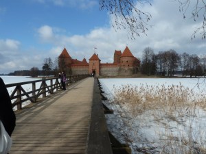 Trakai Island Castle, a red brick castle built on an island. I'm standing on the mainland at the start of a wooden footbridge that stretches across the frozen lake to the gate of the castle.