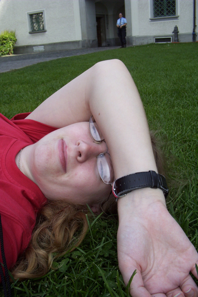 Selfies weren't a "thing" in 2006, but here I am lying in the grass outside the cathedral in St Gallen, taking selfies. I'm lying on my back with my right arm draped over my face. I'm wearing a red t-shirt and a watch with a black strap.