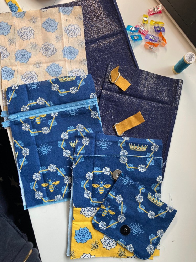 All the pieces of the bag ready to be put together. They're all stubby rectangles in various blue and yellow bee fabrics, except the liners which are glittery navy blue. They're all laid out on my desk with the front on top, the back underneath and the middle at the bottom.
