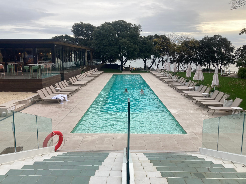 The Nici's outdoor pool, a long off-blue rectangle stretching away from the steps leading to the restaurant. At the end of the pool are some trees and beyond that, the sea and the low winter sun.