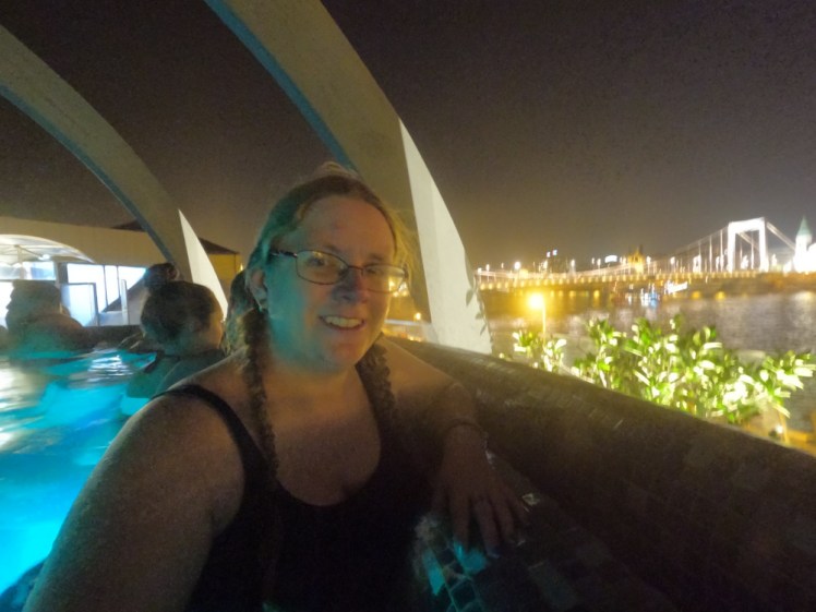A selfie in the hot tub on the roof of Rudas baths. Behind me, there's an illuminated bridge and the lights from the street and behind me are concrete struts forming a kind of crown over the hot tub.