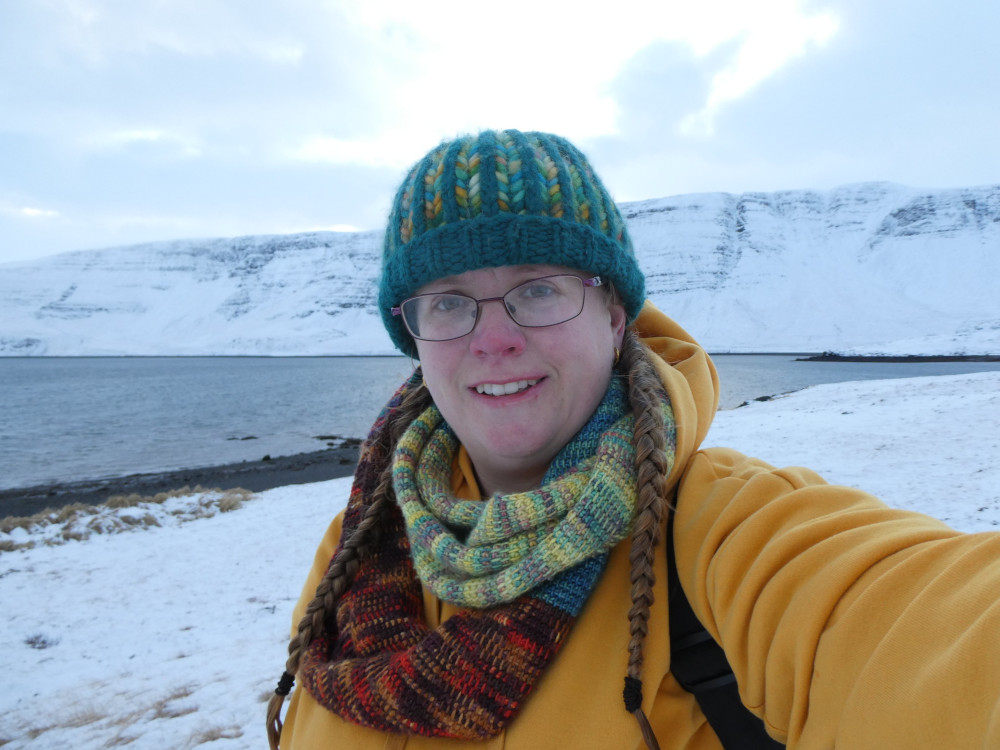 A selfie in colourful knitwear and a yellow hoodie against a snowy scene and dark blue sea.