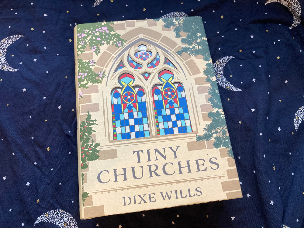 Tiny Churches by Dixe Wills, a hardback book with the cover of the end of a church on it. The stained glass window is actually on the cover of the book itself which shows the altar and the inside of the church.