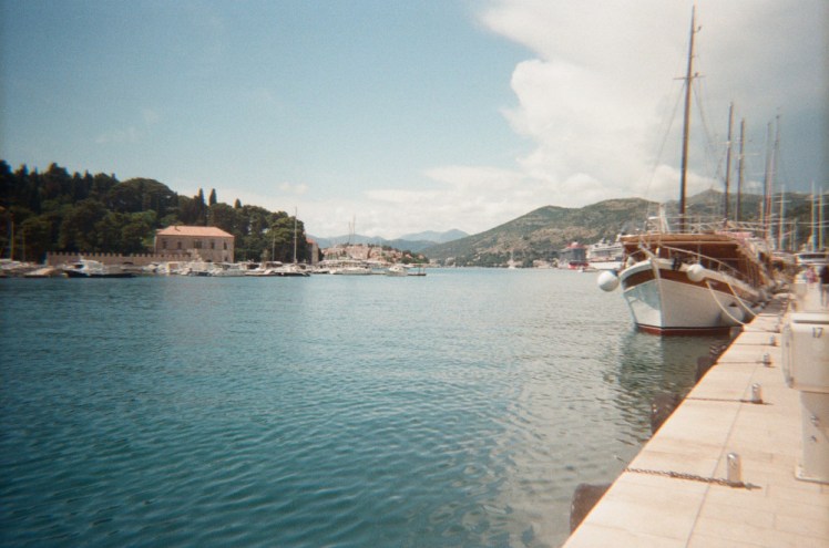 Looking along the quay and out across the water in Croatia. The sea is turquoise, the quay and boats and the villa on the other side all have a slightly beige tint to them.