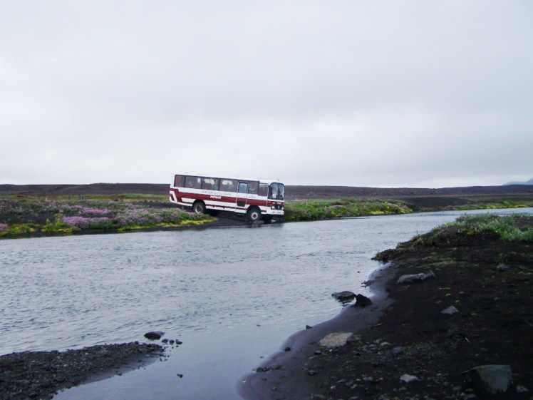 The Asjka expedition coach teetering on the edge of the road, about to drive straight into a river.
