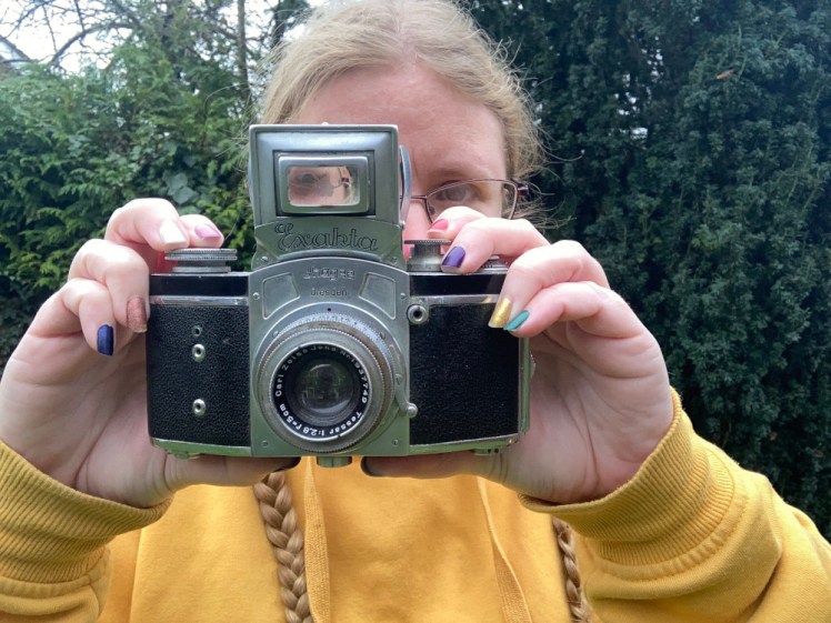 Holding up the last camera, another old-fashioned black & chrome one, this one with a fold-out waist-level viewfinder folded up on top like a little tower so I can look through it while holding it at eye level.