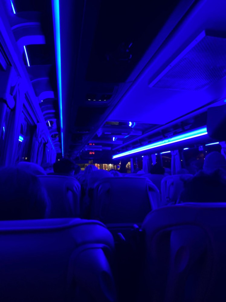 Inside a minibus at night, lit by bright blue tube lights.