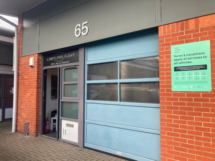 A small industrial unit just wide enough for a roller door to a loading bay and a single door with a vertical row of windows. It has a big number 65 over the whole thing and a smaller Limitless Float logo over the door.
