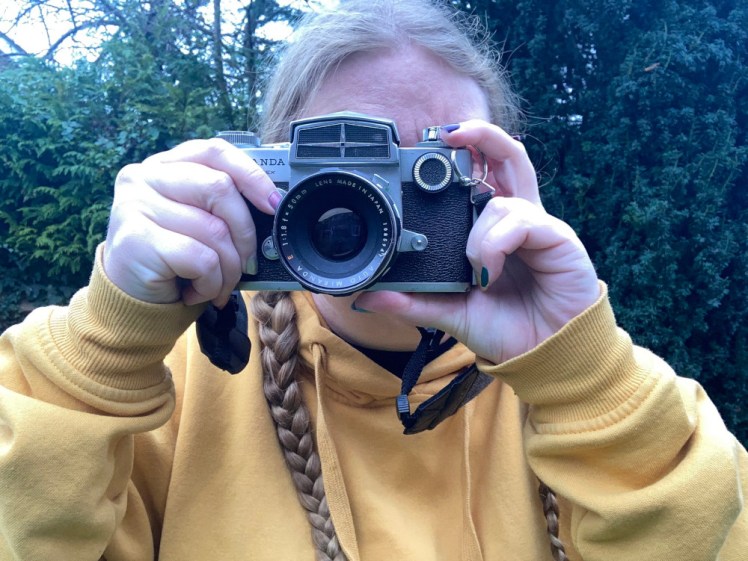 Now holding up a much larger, much heavier and much visibly older camera, with a black and chrome body and a large removable lens. I'm holding down the shutter button with my right forefinger; it's on the front right next to the lens.
