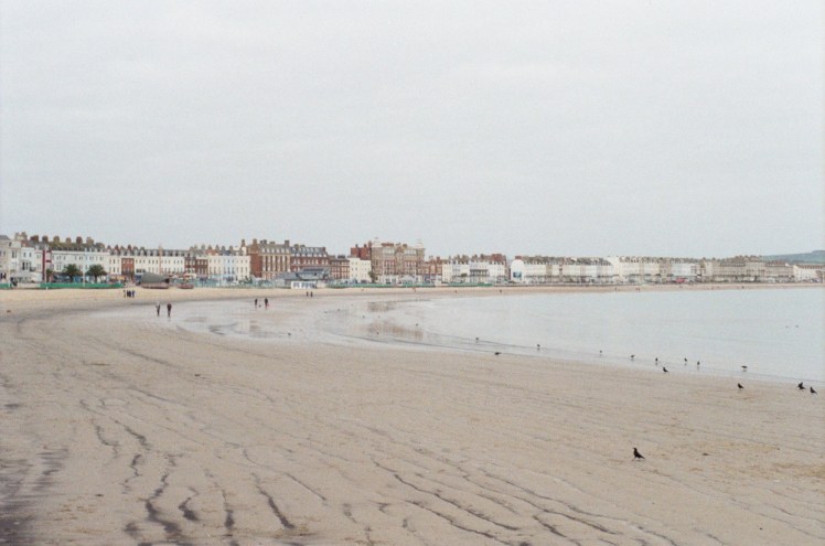 An overexposed photo of Weymouth beach, which is all very pale shades of beige-orange and very light blue. This was taken on the Miranda, which wants to have its exposure adjusted but is too old for me to do so.