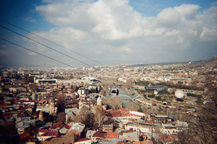 Tbilisi seen from around the Mother of Georgia. The colours are a little unsaturated and there are dark shadows in three corners of the picture.