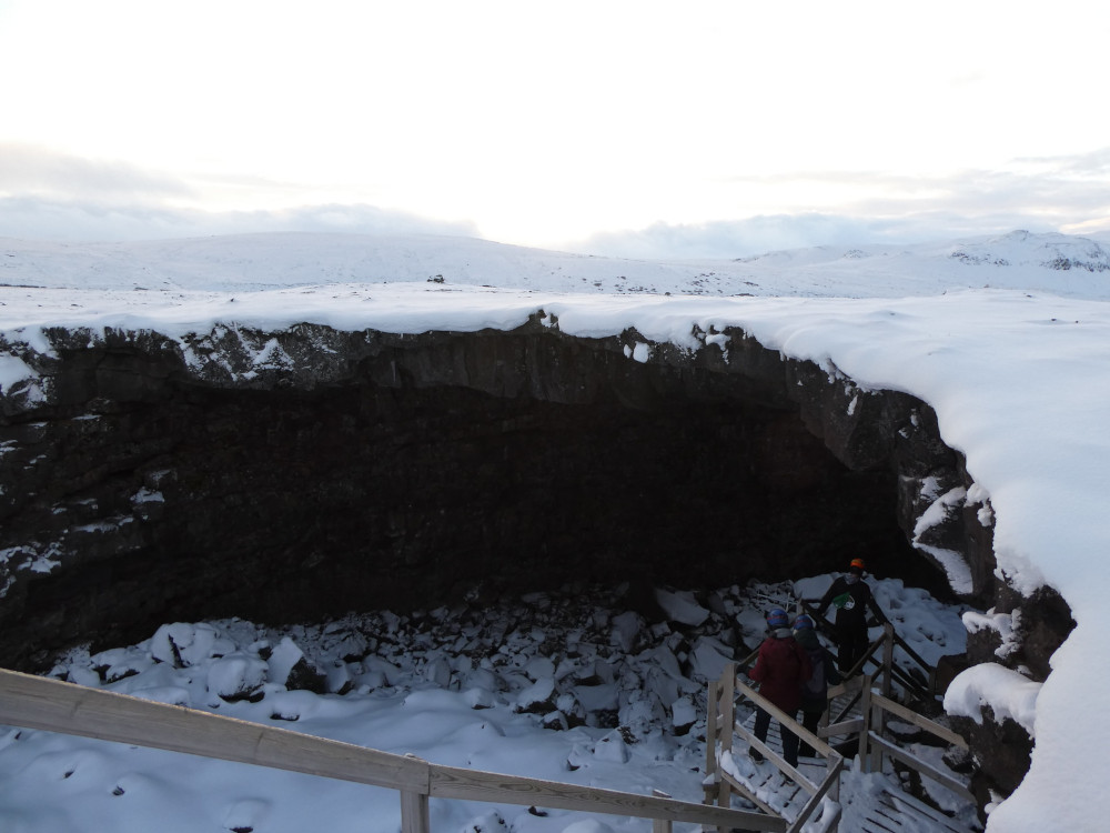 A huge pit in the snowy landscape with wooden steps winding down one side of it. The roof of the cave is at least a foot thick, two feet in places.