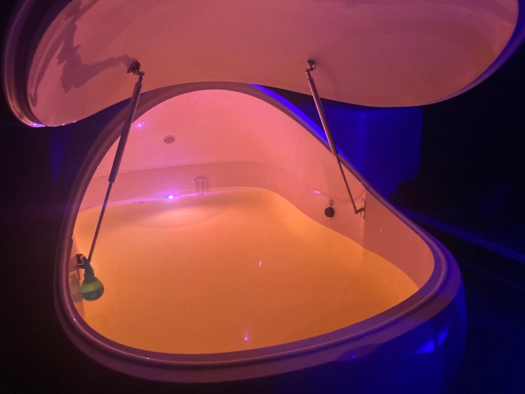 The tank, a kind of space-age curved white plastic thing with a raised lid. The outside is dimly lit in blue but the inside of the tank is lit in a pinkish-orange light which disguises the fact that the water, which half-fills the tank, is slightly yellow.