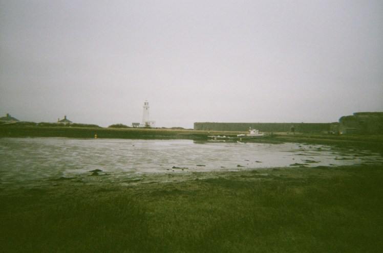 A view across the hook-shaped end of the Spit, with a bit of marshy water separating me from the lighthouse and castle on the other side of the hook.