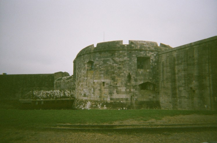 The older part of Hurst Castle, a two-storey round stone castle, a little wider than it is tall, with walls the same height sticking out both sides.