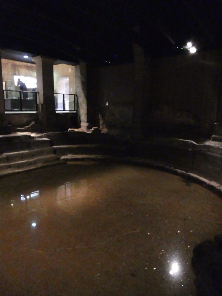 The men's cold bath, with some water in it. There are steep steps down from the opposite side and presumably the bath would have been filled a lot more than this.