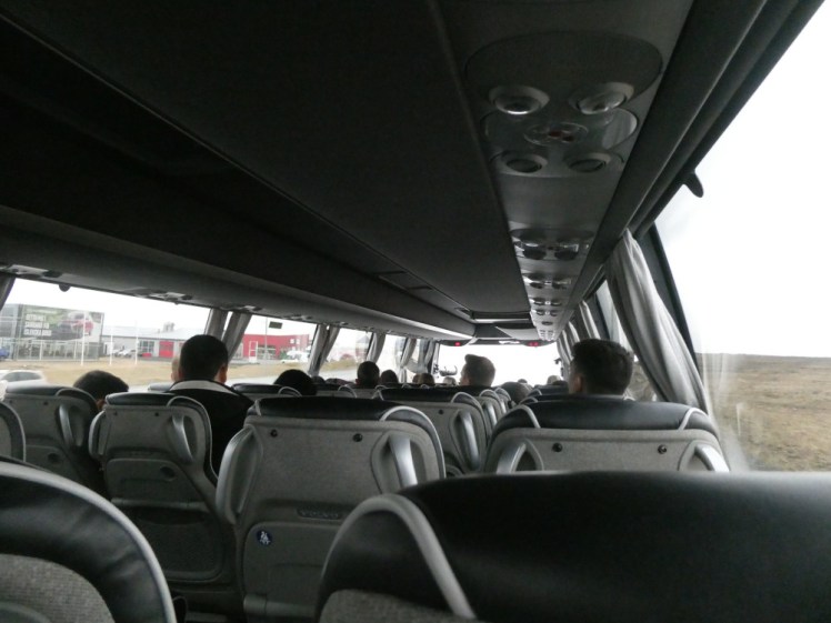 A view down the inside of the airport bus from somewhere near the back. It's actually a well-maintained executive coach, with leather seats and overhead chargers and lights.