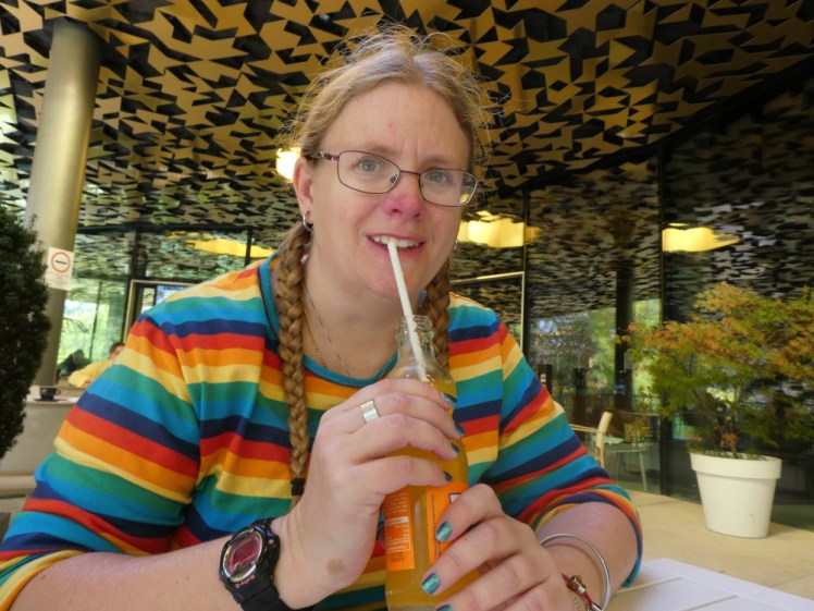 In a cafe in Budapest, with a bottle of Fanta and a straw, wearing my bright rainbow-striped top.