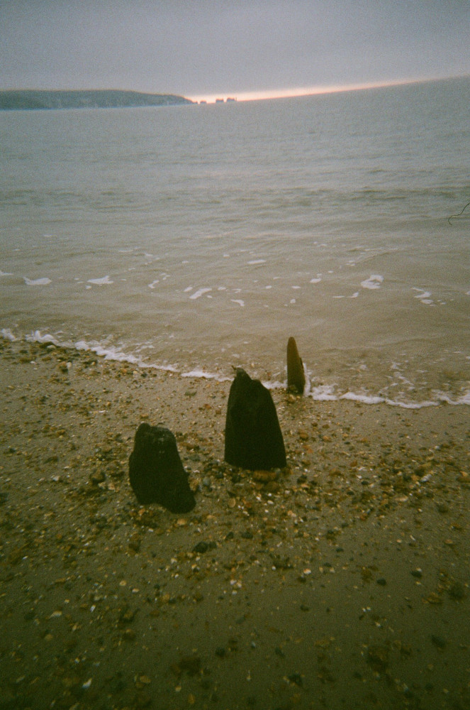 Three standing stones, right on the edge of the shingle shore, washed with the waves. The biggest of the stones is maybe 18 inches tall and about half that width.