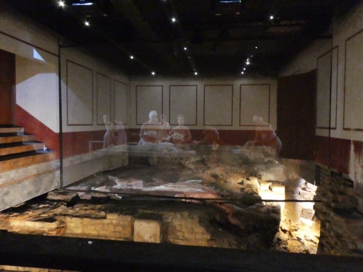 The remains of the hot room at the women's end of the complex, with white and red panelling clearly added fairly recently. The Roman floor and hypocaust is enhanced by a projection showing women lounging, being massaged and scraped etc.