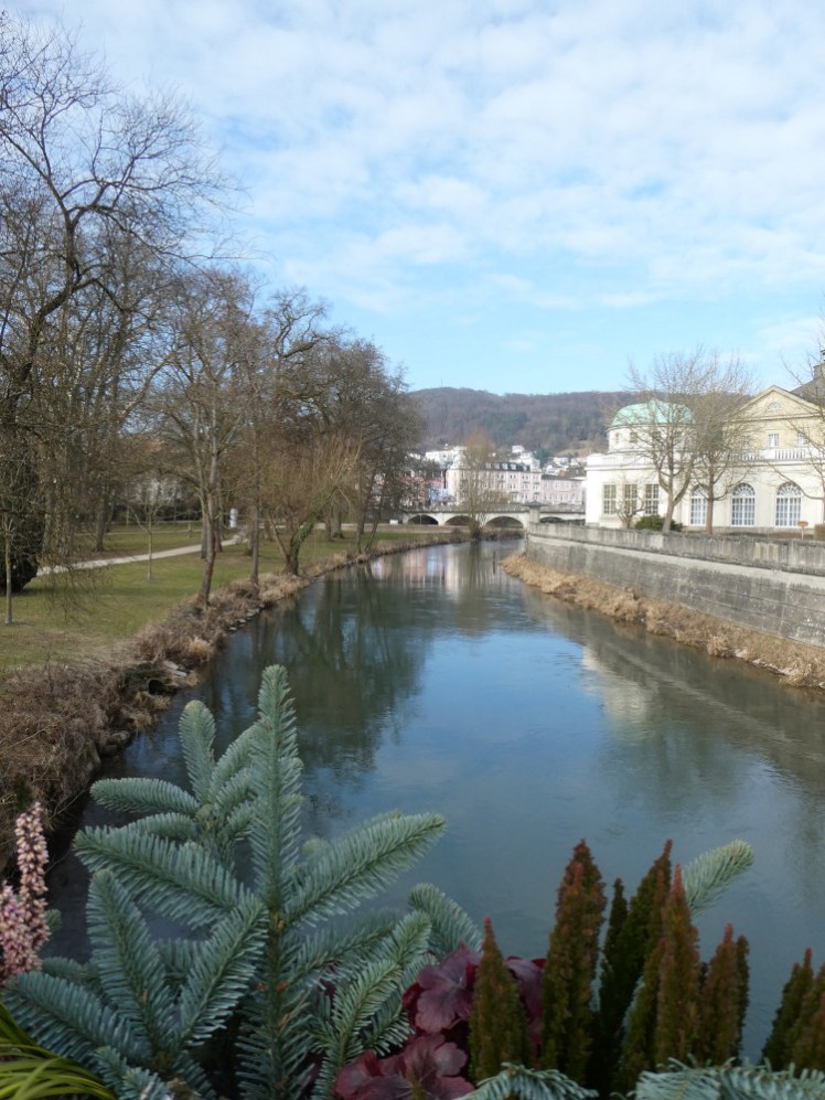 Looking up the river from a bridge with trees and park on the left and the Kurhaus on the right.