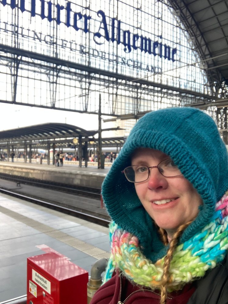 A selfie at Frankfurt, wearing a teal-blue knitted hood and pastel scarf. I clearly have plenty of time to mess around taking selfies rather than running for a train.